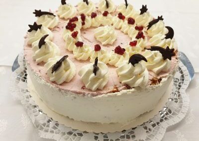 Festlich dekorierte Buchweizentorte mit Sahnetupfen, Schokoladendeko und roten Beerenstückchen