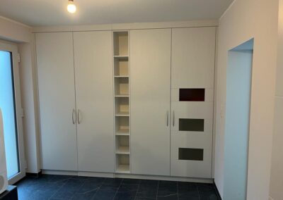 Großer weißer Einbauschrank mit mittigem Regalteil und drei Glasfronten in Rot, Grau und Schwarz
