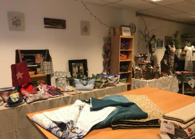 Raum mit genähten Taschen, Decken, Stoffen und Dekoartikeln auf Tischen und Regalen