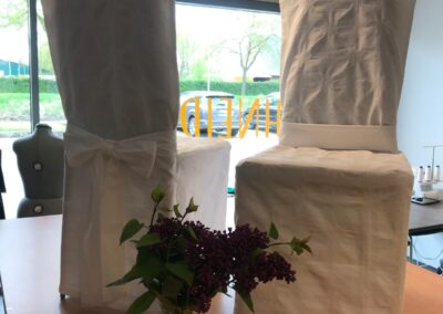 Zwei Stühle mit weißen Hussen und Schleife neben einem Blumenstrauß auf einem Holztisch im Atelier