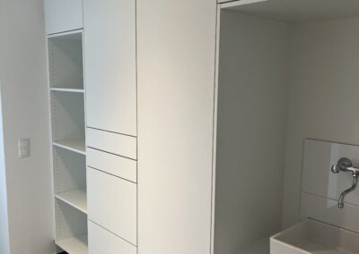 Moderner weißer Einbauschrank mit offenen Regalen und integriertem Waschplatz in einem funktionalen Raum