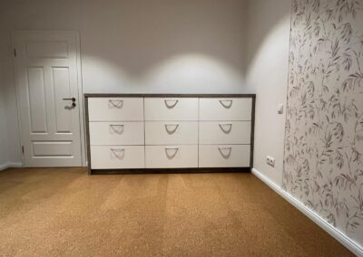 Weiße Kommode mit neun Schubladen und grauem Rahmen in einem hellen Raum mit Teppichboden