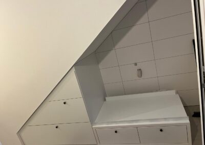 Weißer maßgefertigter Schrank unter einer Dachschräge mit Schubladen und Fliesenwand