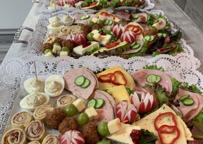 Reich belegte Schnittchen-Platten mit Käse, Wurst, Eiern, Trauben, Frikadellen und Radieschendeko auf Spitzendeckchen