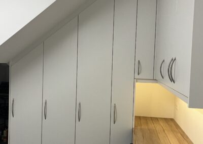 Weißer Einbauschrank unter einer Dachschräge mit integrierter Holzarbeitsplatte und Oberschränken