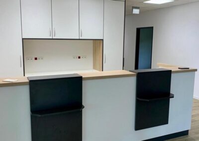 Weiße Empfangstheke mit Holzarbeitsplatte und schwarzem Frontaufsatz vor einem Einbauschrank in einer modernen Praxis oder einem Büro
