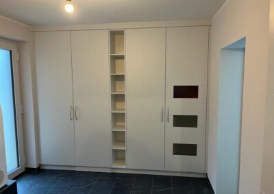 Weißer, deckenhoher Einbauschrank mit offenem Mittelregal und drei Glaseinsätzen in Rot und Grau in modernem Innenraum