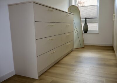 Beigefarbene Kommode mit goldenen Griffen in modernem Ankleidezimmer